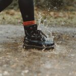 Close-up of waterproof boots splashing through a puddle on a rainy day outdoors.