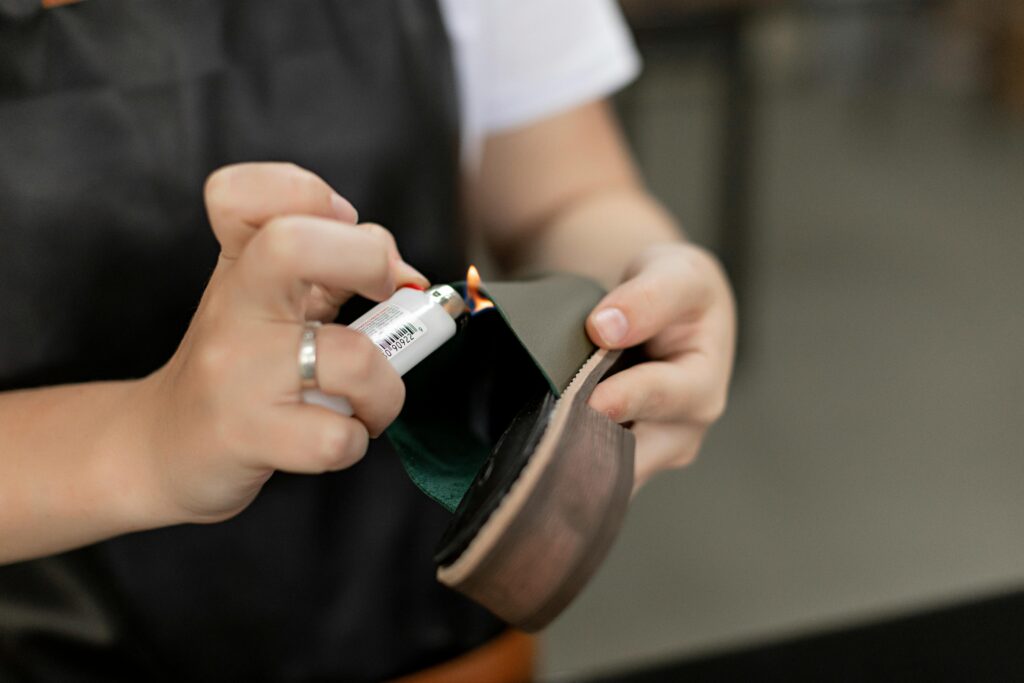 Detail of hands using a lighter for handmade shoe repair in a workshop.